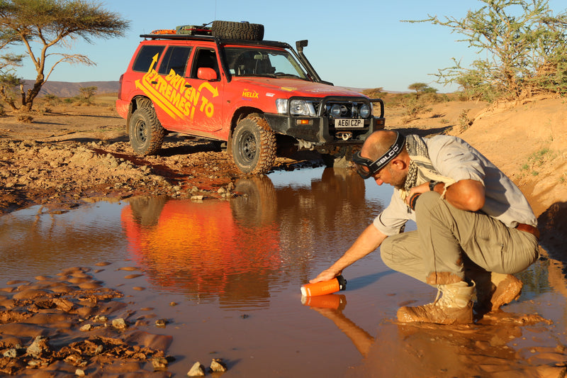 Load image into Gallery viewer, Person refilling LifeSaver Liberty bottle from a muddle puddle by a red off-road vehicle in a desert setting
