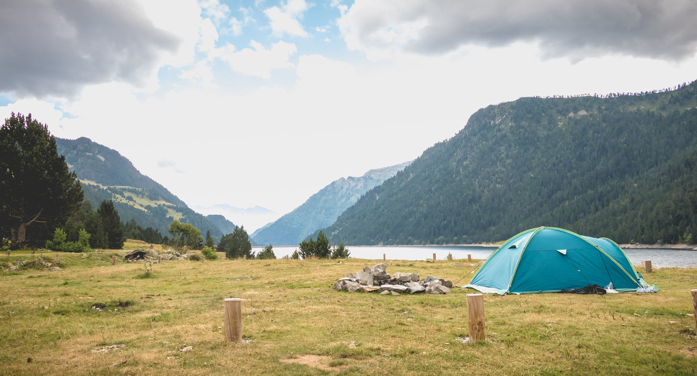 Blue tent set up in a grassy area with mountains and a lake in the background