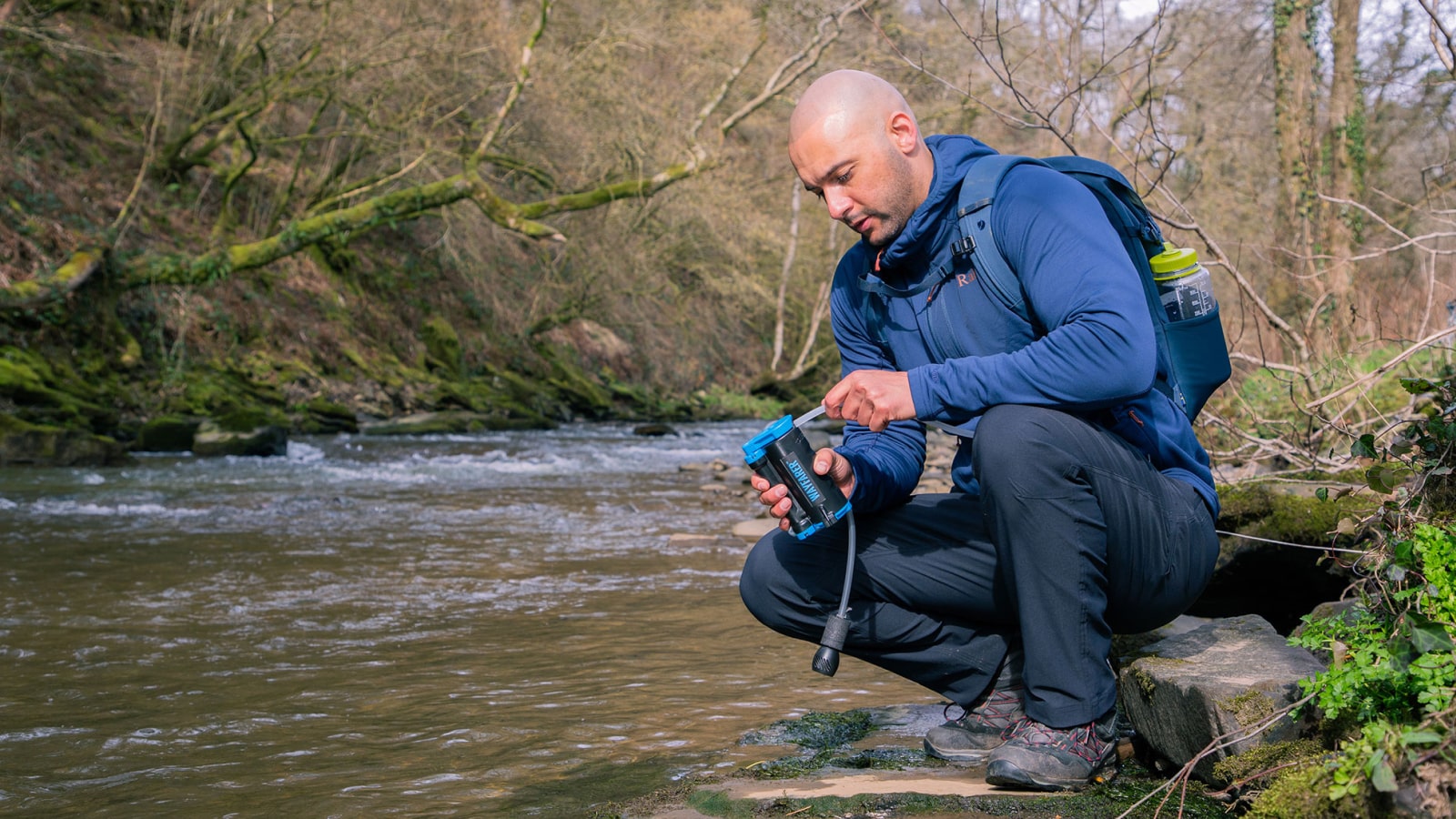 Man with a backpack filtering water from a stream in a natural setting